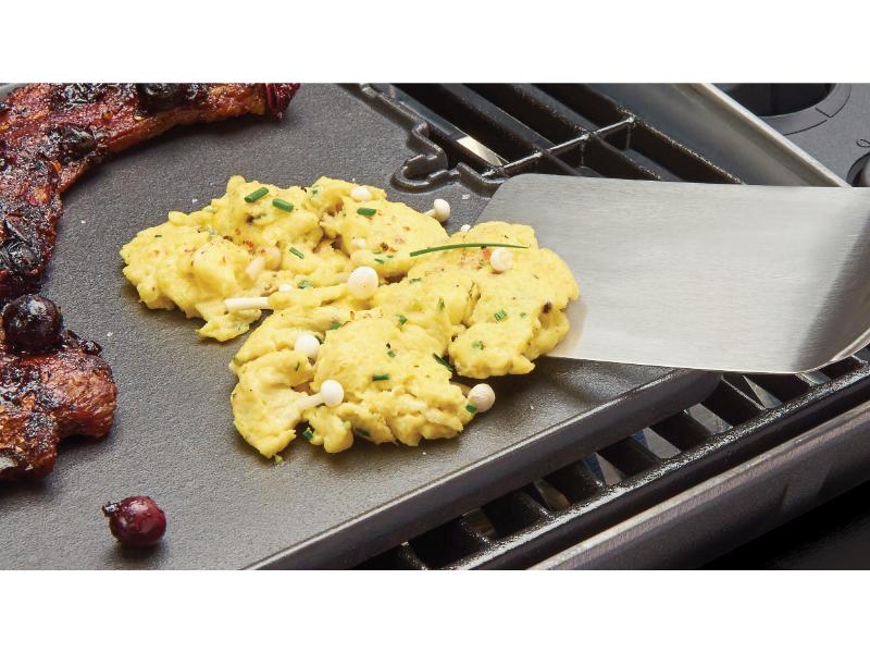 Scrambled eggs on a griddle with a spatula and meat beside them