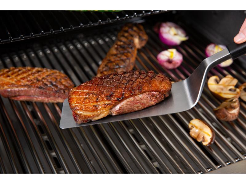 Grilled steak being turned on a barbecue with vegetables.