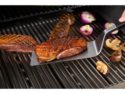 Grilled steak being turned on a barbecue with vegetables.