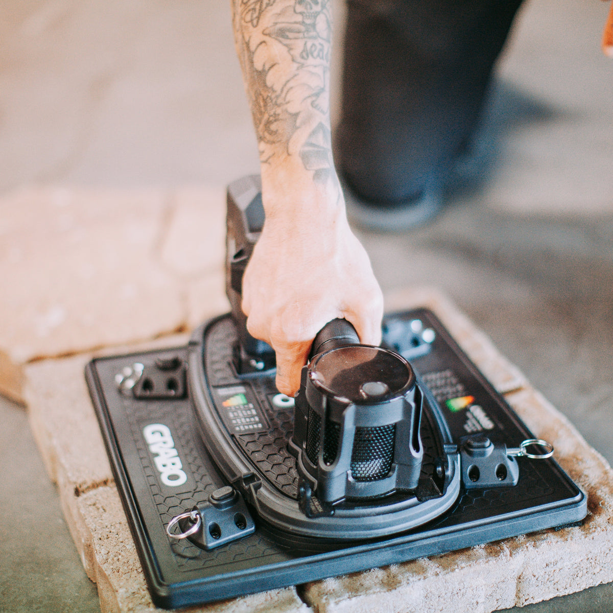 A close-up of a person's tattooed arm and hand operating a black and gray wet/dry floor drain assembly on a concrete floor.