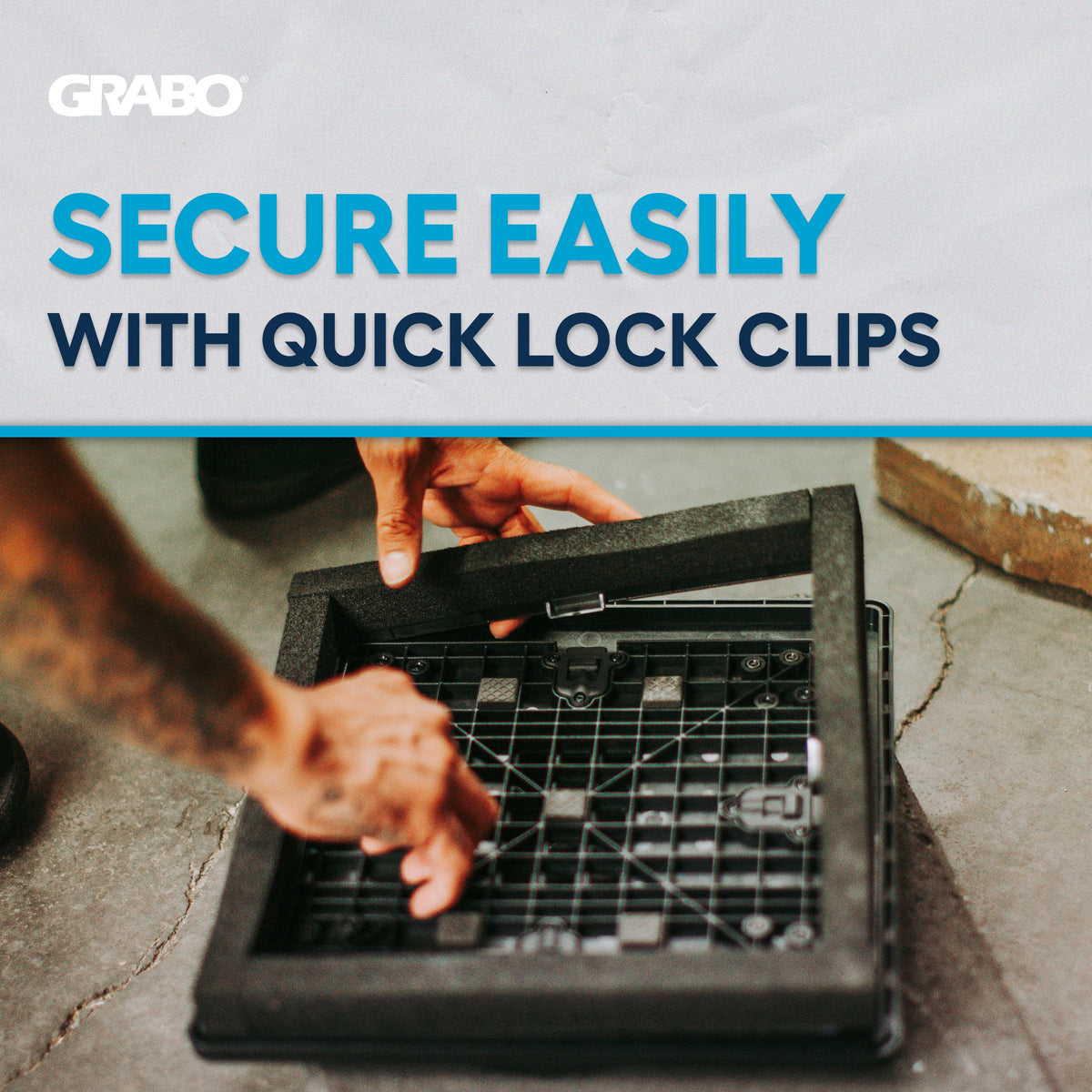 A close-up of a person's hands installing a black quick lock clip onto a gray concrete floor, with a white banner at the top featuring the text 'GRABO SECURE EASILY WITH QUICK LOCK CLIPS'.
