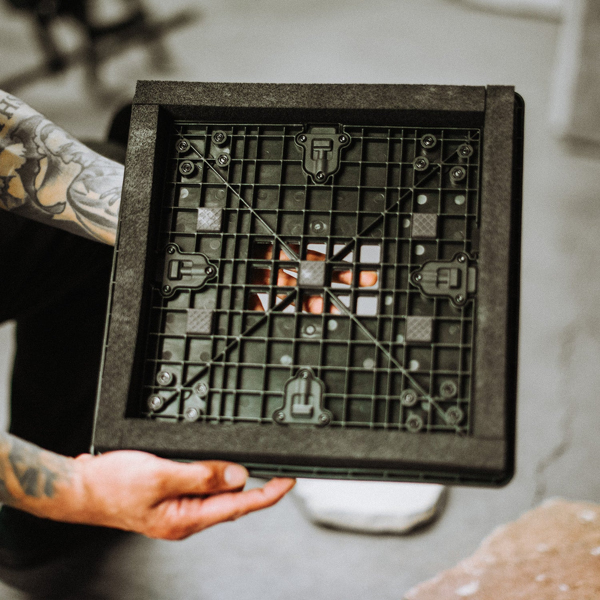 Person holding a black square object with grid pattern and small figures on a neutral background