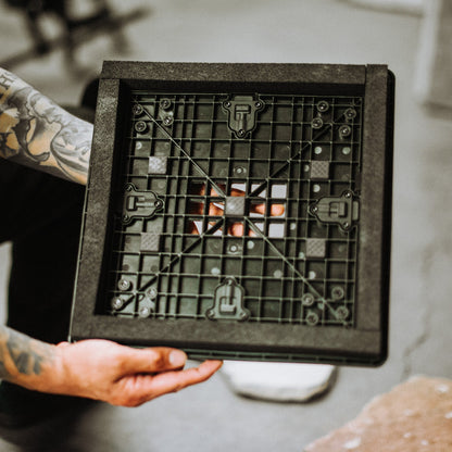 Person holding a black square object with grid pattern and small figures on a neutral background