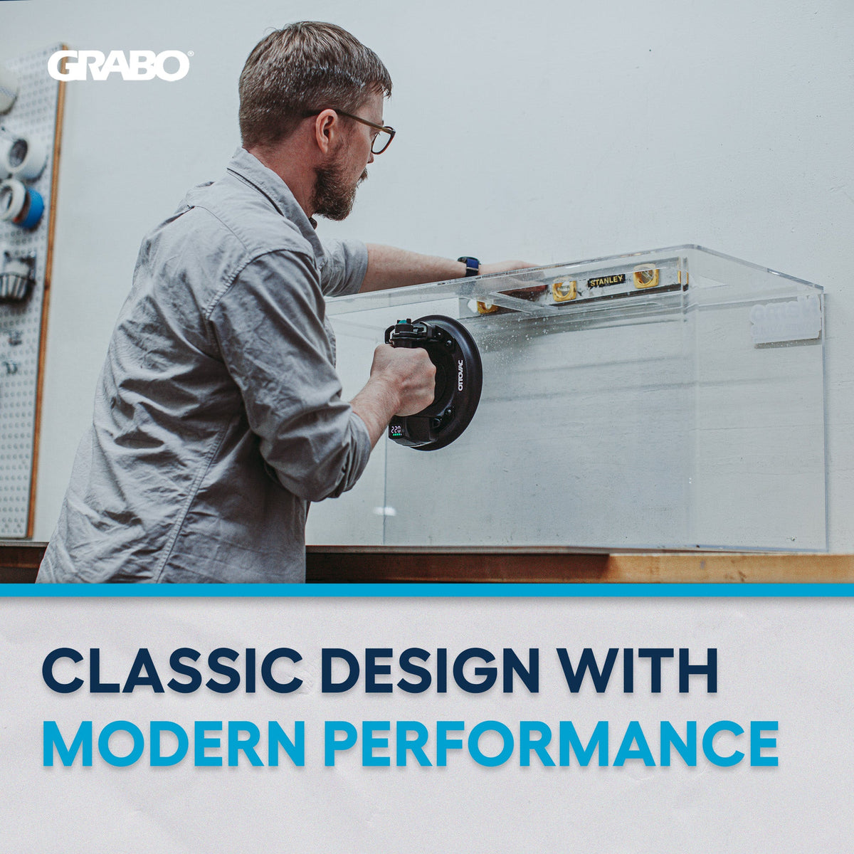 A man in a gray shirt and glasses uses a black circular Grabo tool on a clear acrylic panel inside a workshop. The image features a white banner at the bottom with the text 'CLASSIC DESIGN WITH MODERN PERFORMANCE' and the Grabo logo in the top left corner.
