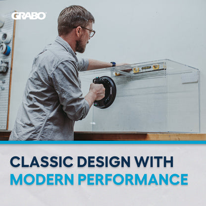 A man in a gray shirt and glasses uses a black circular Grabo tool on a clear acrylic panel inside a workshop. The image features a white banner at the bottom with the text 'CLASSIC DESIGN WITH MODERN PERFORMANCE' and the Grabo logo in the top left corner.